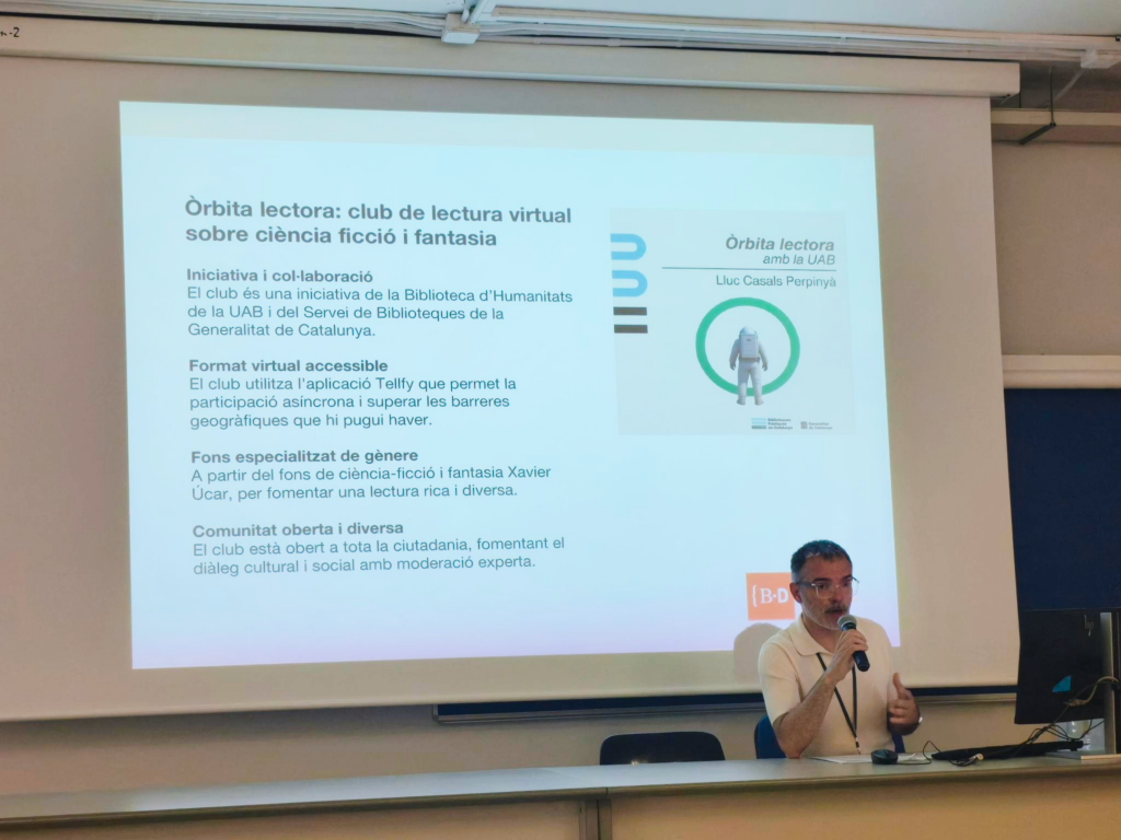 En Raul Coré parla amb un micròfon davant d'una pantalla que projecta una diapositiva informativa sobre l'«Òrbita lectora: club de lectura virtual sobre ciència-ficció i fantasia».